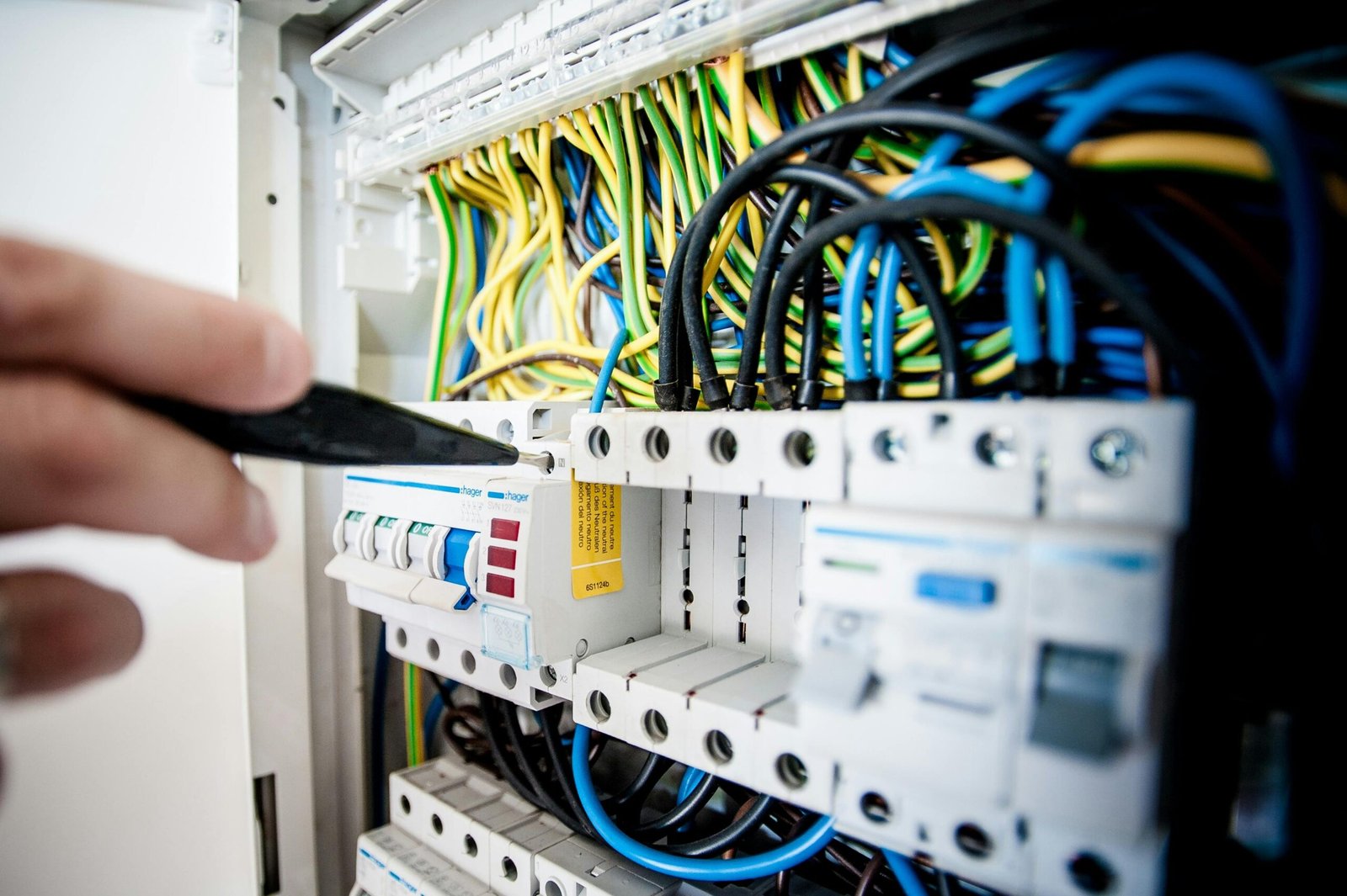 Hand of electrician working on a circuit breaker panel with colorful wires, ensuring safe electrical connections.